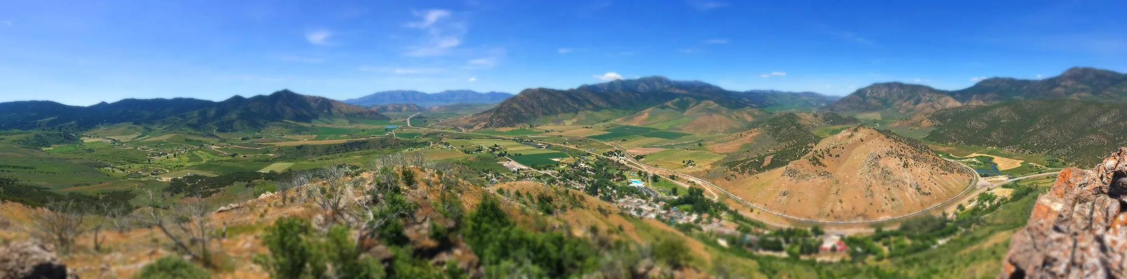 Panorama of the Lava Hot Springs valley in summer — green fields, the river bend, mountains on every side
